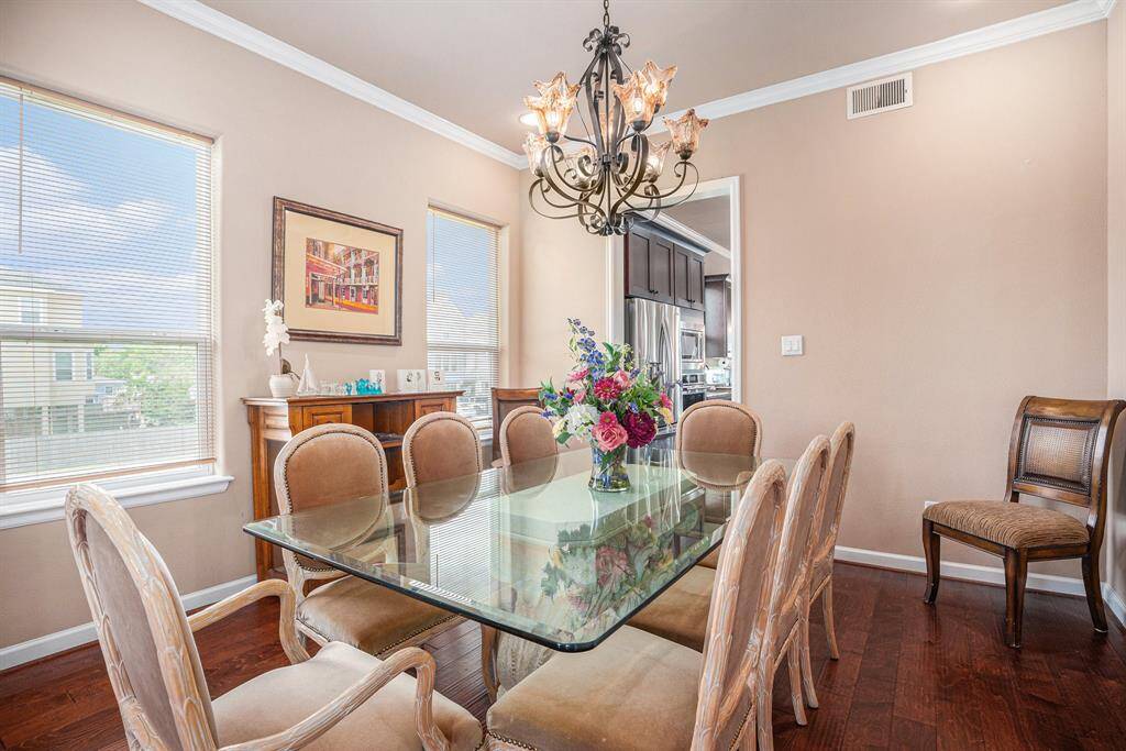 A formal dining room boasts a glass-top table with eight cushioned chairs, a chandelier, and a wooden buffet shelf with decor.