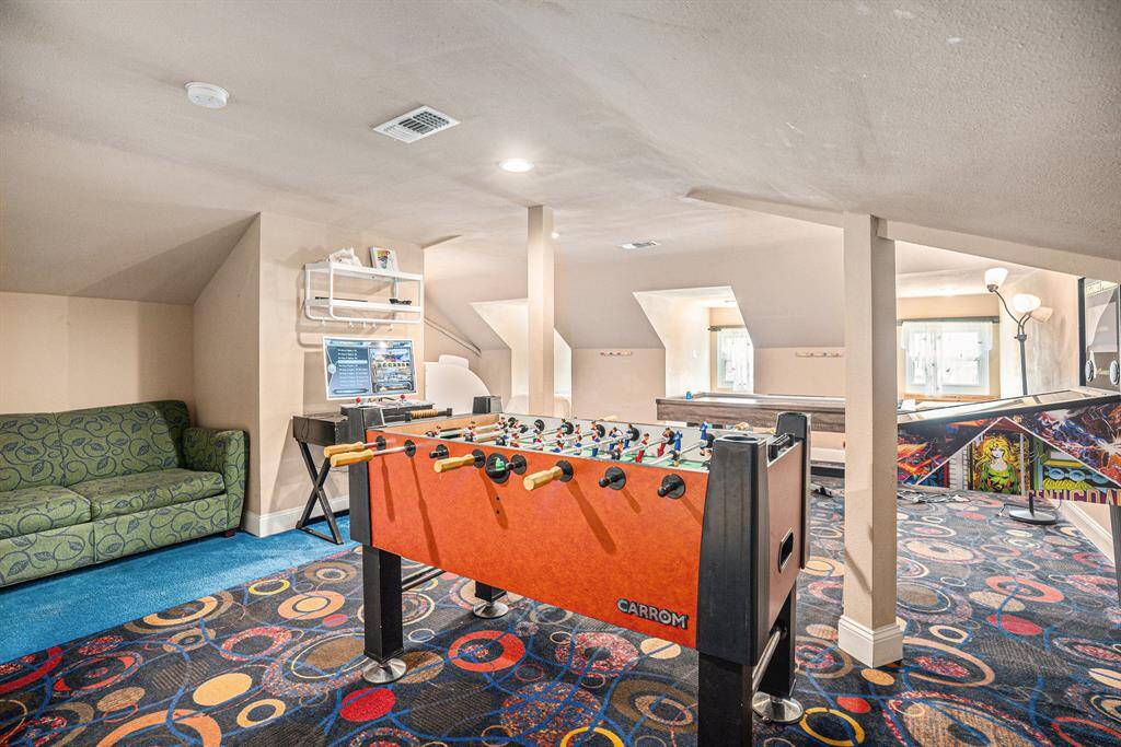 Dive into a thrilling bonus room on the fourth floor packed with endless entertainment, showcasing a Carrom foosball table, retro arcade machine, cozy green sofa, three built-in bed areas, and a bunk bed around the corner, all in a burst of vibrant color!