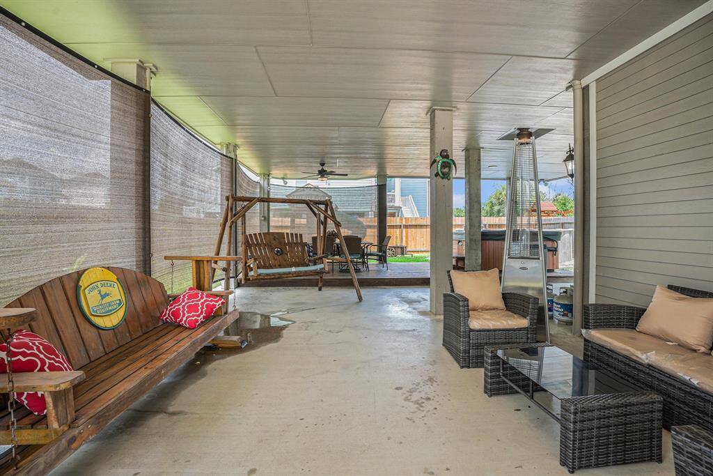 spacious covered patio with wooden swings, cushioned seating, outdoor blinds for shade, and a view of a backyard, creating a cozy and inviting outdoor living space.