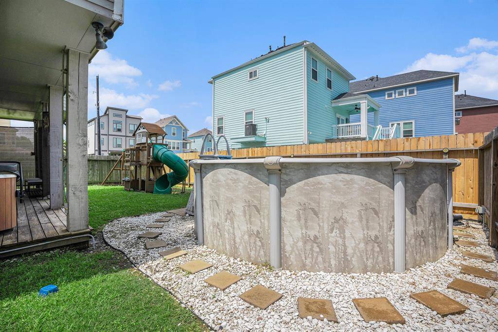 Check out the playset and slide, an above-ground pool surrounded by a stone pathway, and a wooden privacy fence, all under a clear blue sky.