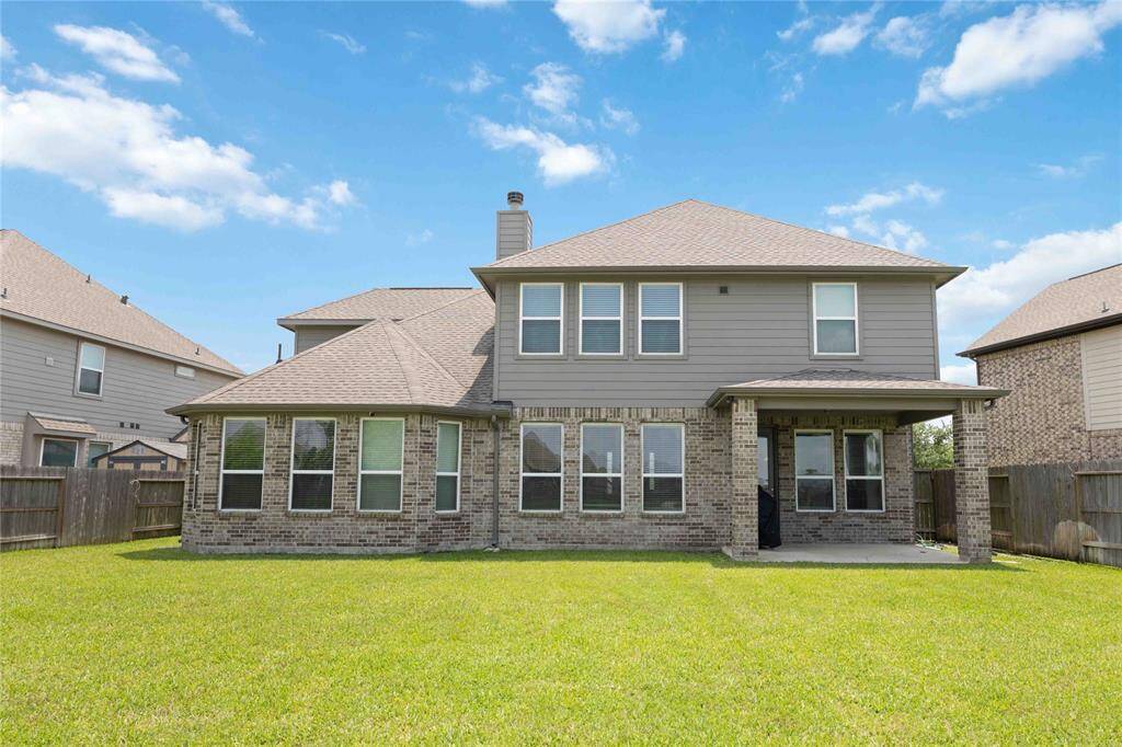 This photo showcases a two-story home with a brick facade and multiple large windows, providing ample natural light. It features a spacious backyard with a well-maintained lawn, ideal for outdoor activities. The patio area offers a perfect space for relaxation or entertaining guests.