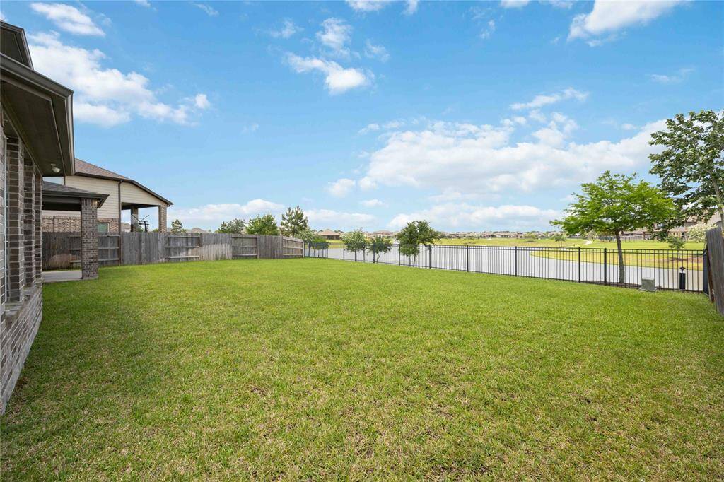 Spacious backyard with lush grass, bordered by a wooden fence on the sides and a wrought-iron fence overlooking a serene water view. Ideal for outdoor activities and enjoying scenic landscapes.