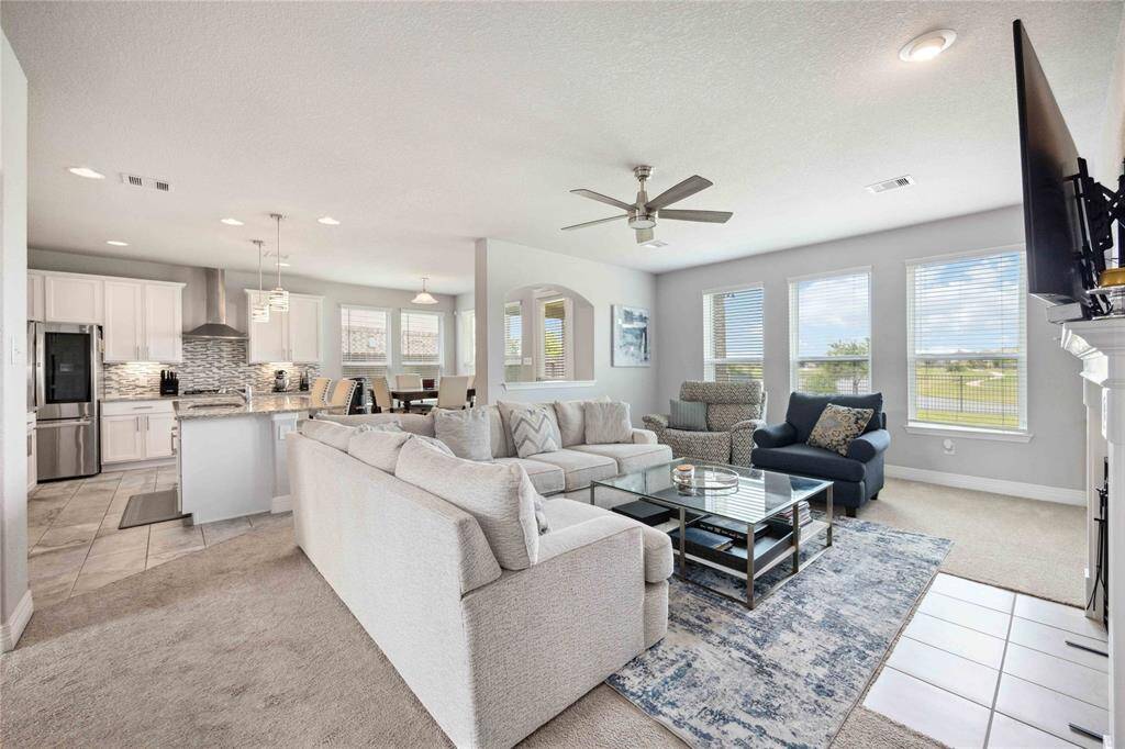 This open-concept living area features a spacious, light-filled room with modern decor and a fireplace. The adjacent kitchen boasts sleek cabinetry, stainless steel appliances, and a stylish backsplash. Large windows offer plenty of natural light and a scenic view.