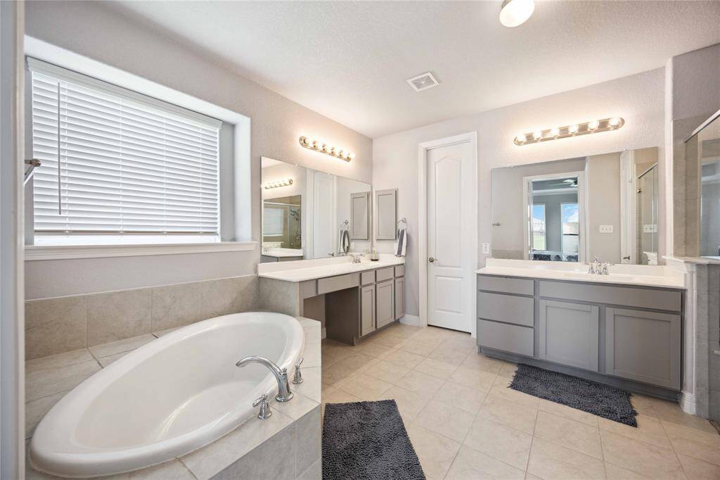 This spacious primary bathroom features a large soaking tub, dual vanities with ample counter space, modern fixtures, and a separate shower. Neutral tones and bright lighting create a clean, inviting atmosphere.
