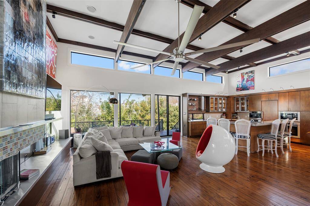 The modern living area features 14ft high ceilings with exposed wooden beams and abundant natural light. The open layout connects a cozy seating area with a stylish kitchen, offering a perfect blend of comfort and elegance.
