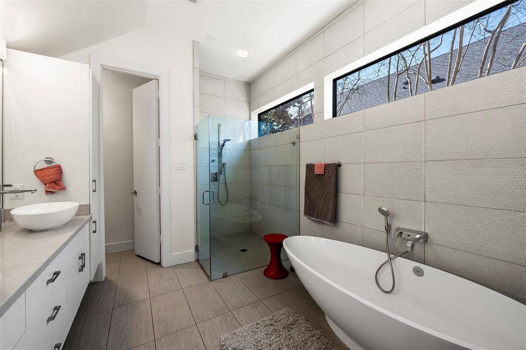 The primary bathroom features a sleek soaking bathtub, glass-enclosed shower and dual vanity sinks.