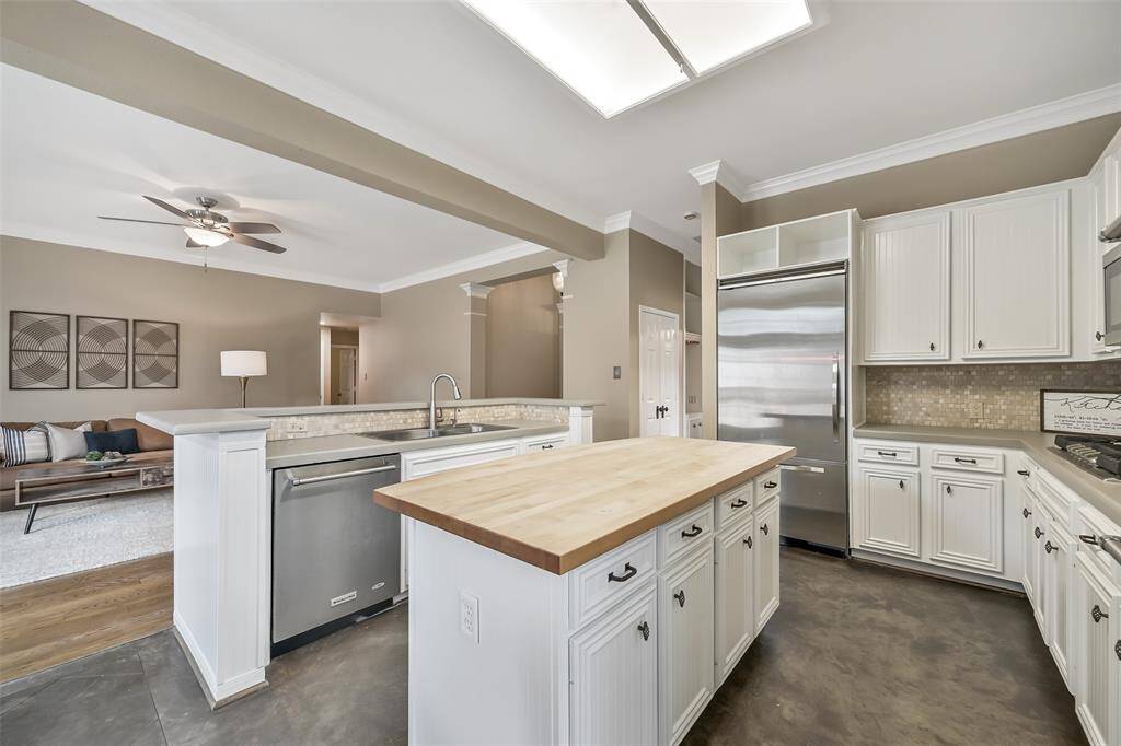 The heart of the home features freshly painted cabinetry, durable concrete countertops, a butcher block island, breakfast bar seating space, and stainless appliances, including a Viking built-in fridge—all open to the living space for effortless entertaining.