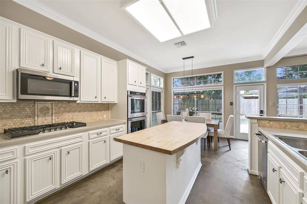 The light and bright kitchen with stainless appliances, concrete countertops, a mosaic tile backsplash, and butcher block island flows into a sunlit dining area with modern pendant lighting and direct access to the backyard.