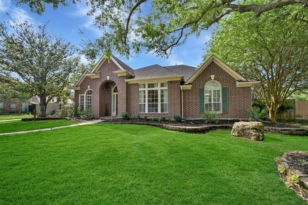 Charming red brick elevation with arched windows, lush landscaping, and a graceful front entry framed by mature shade trees—all set on a beautifully maintained lot in Wilderness Trails.