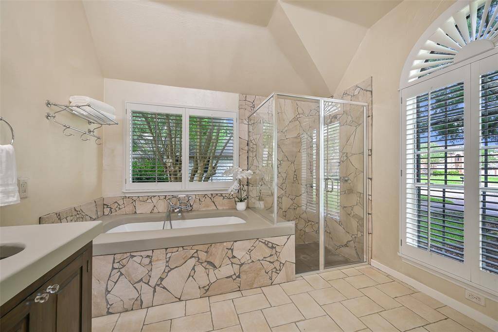 Unwind in the luxurious bubbler tub framed by striking stone tilework, with a separate glass-enclosed shower and oversized windows with plantation shutters - bringing in natural light without forsaking privacy.