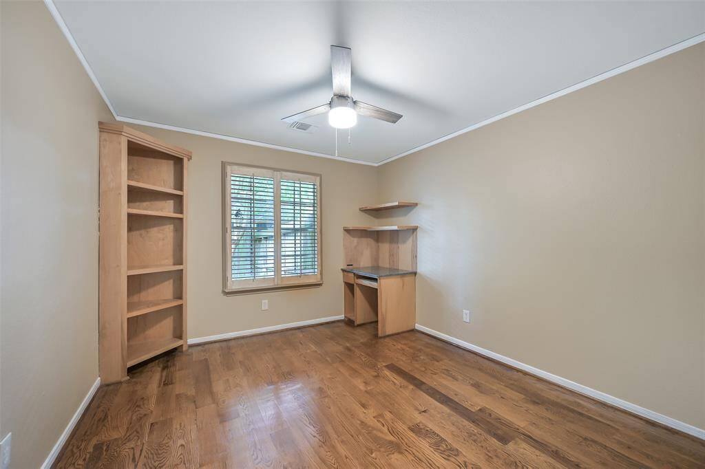 This secondary bedroom features handsome wood floors, a side-facing window with plantation shutters, a double door closet, built-in shelving, and a corner desk—ideal for a student workspace or home office.