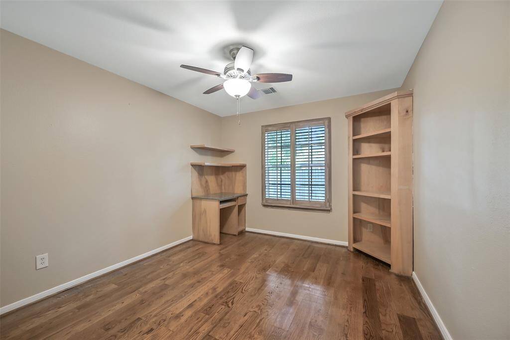 The fourth and final bedroom in the home is just like the previous room, also offering wood floors, a side-facing window with plantation shutters, a double door closet, built-in shelving, and a corner desk—ideal for a student workspace or home office.