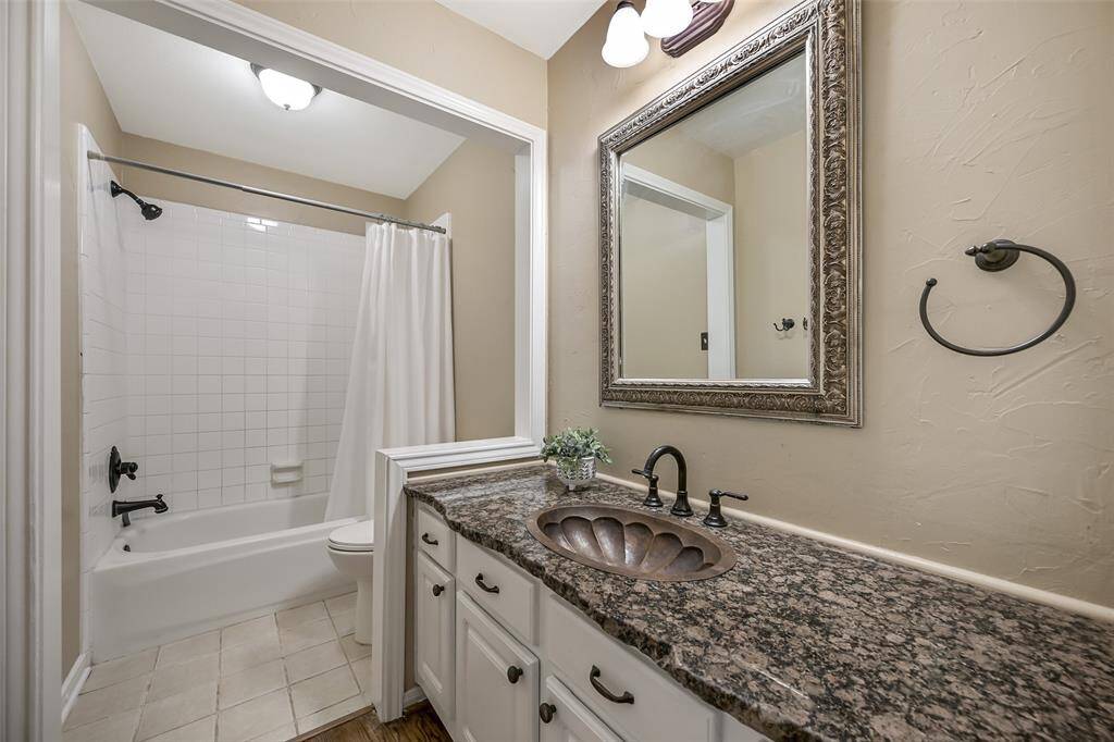 The hall bath features a raw edge granite-topped vanity with a decorative copper sink, oil-rubbed bronze fixtures, a framed mirror, and a classic tub/shower combo with a crisp white tile surround.