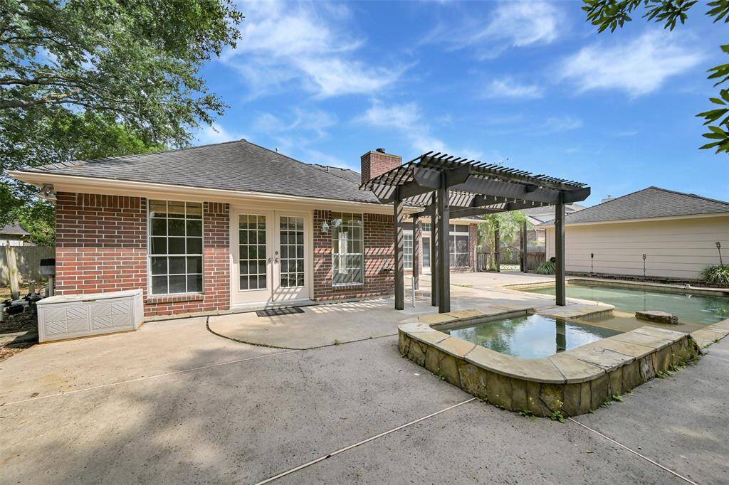 French doors from the spacious game room lead to a private backyard oasis with a sparkling pool and elevated spa, all beneath a stylish pergola—perfect for entertaining or relaxing in the shade.