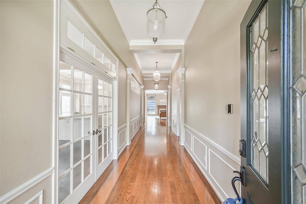 Step through the solid mahogany and leaded glass front door into a grand hallway with rich wood floors, crisp wainscoting, ornate moldings, and soaring 12-foot ceilings, flanked by French doors leading to the study or formal space.