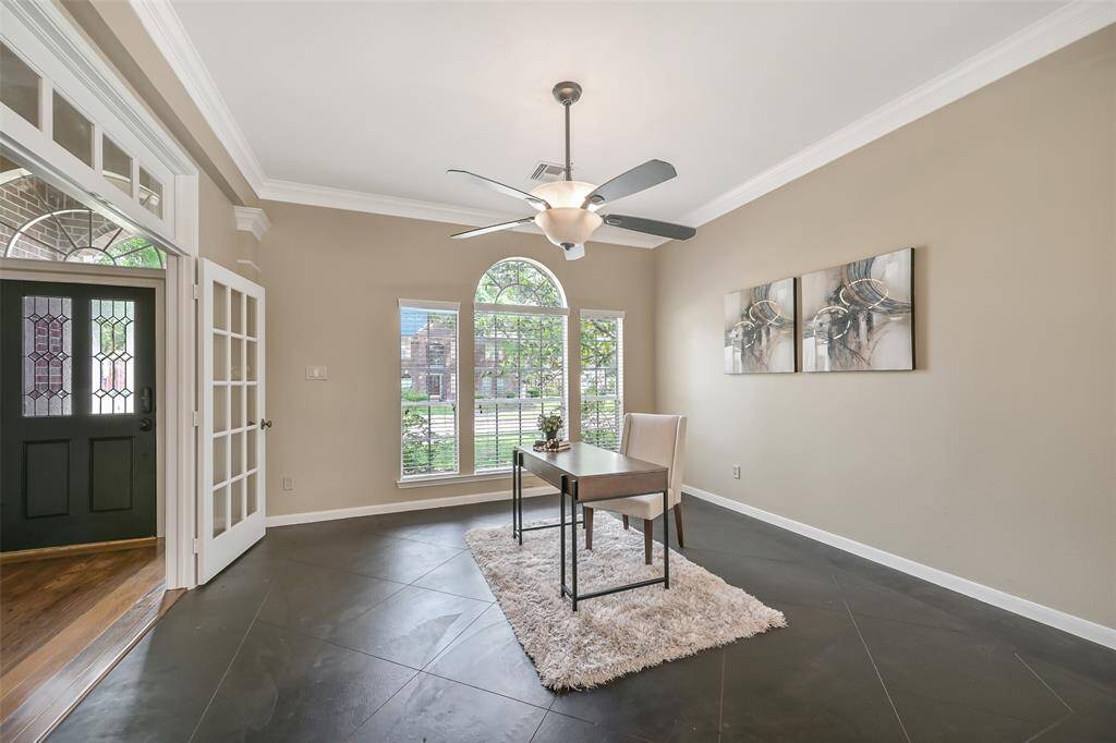 French doors lead into this versatile front-facing room with scored concrete flooring, crown molding, a ighted ceiling fan, and a large arched window that fills the space with natural light—ideal as a study, formal living, or flexible home office.