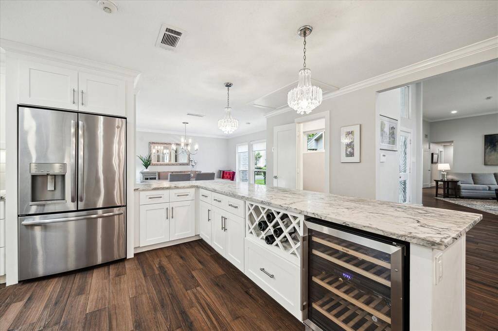 Stainless-steel appliances flank an expansive island beneath recessed and pendant lighting, while rich wood-look tile flooring flows seamlessly into the breakfast nook and living areas.