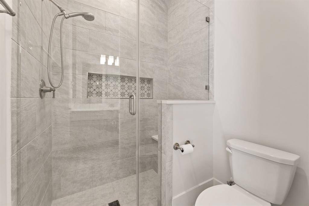 Modern bathroom with sleek dark cabinetry, a large mirror, and a stylish light fixture. Features a glass door leading outside, offering natural light and easy access.