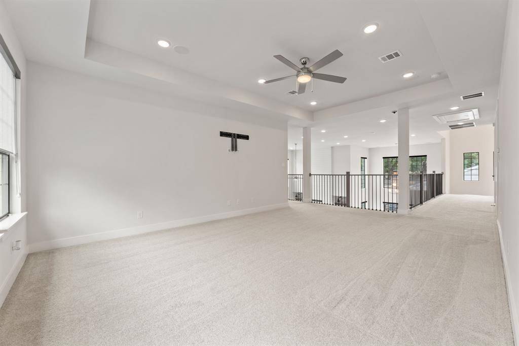 Spacious upstairs game room perfect for entertainment and relaxation. Features three large windows for natural lighting, modern railing overlooking the lower level and connects to adjacent rooms, offering versatile living space.