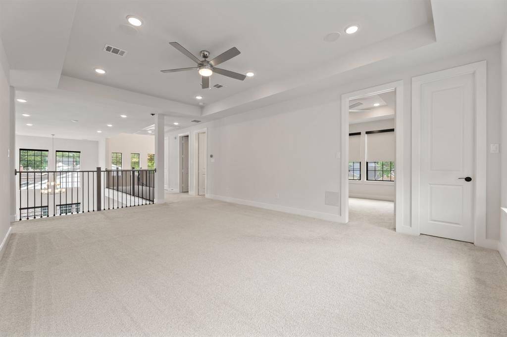 Spacious upstairs game room perfect for entertainment and relaxation. Features three large windows for natural lighting, modern railing overlooking the lower level and connects to adjacent rooms, offering versatile living space.