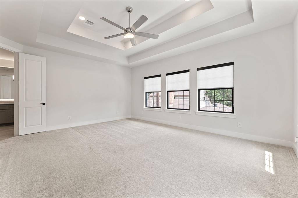 Spacious primary bedroom featuring plush carpeting, a stylish double tray ceiling with a modern fan, and abundant natural light. Direct access to a luxurious ensuite bathroom enhances comfort and convenience.