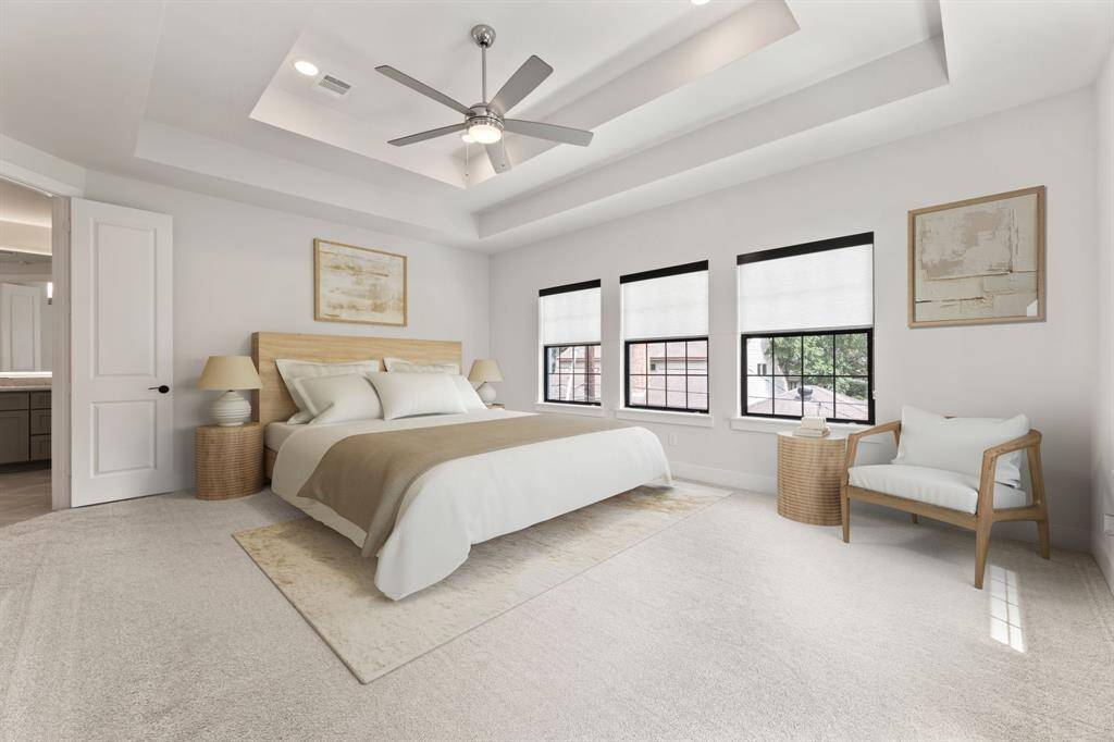 Spacious primary bedroom featuring plush carpeting, a stylish double tray ceiling with a modern fan, and abundant natural light. Direct access to a luxurious ensuite bathroom enhances comfort and convenience.