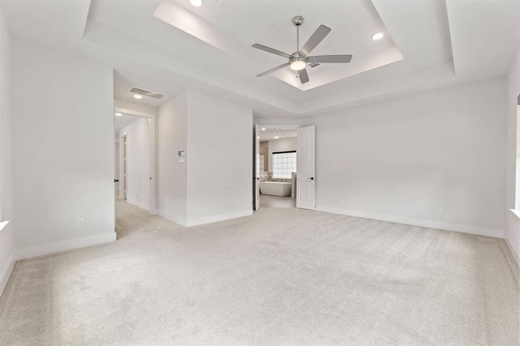 Spacious primary bedroom featuring plush carpeting, a stylish double tray ceiling with a modern fan, and abundant natural light. Direct access to a luxurious ensuite bathroom enhances comfort and convenience.