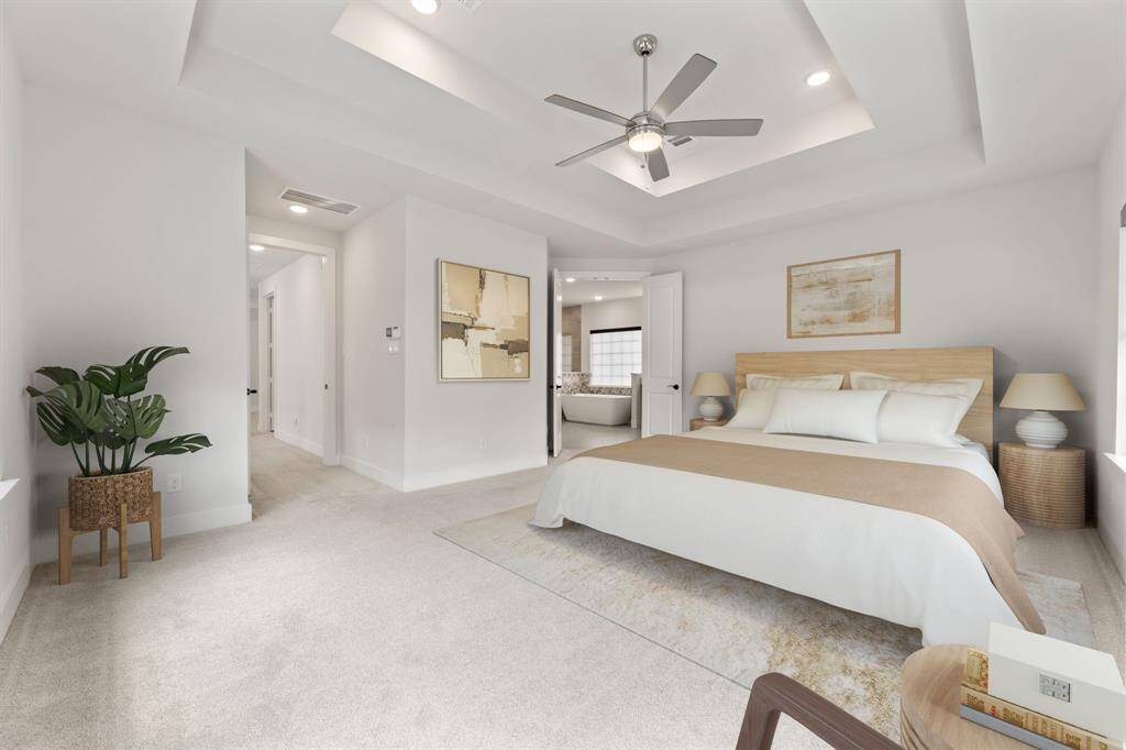 Spacious primary bedroom featuring plush carpeting, a stylish double tray ceiling with a modern fan, and abundant natural light. Direct access to a luxurious ensuite bathroom enhances comfort and convenience.