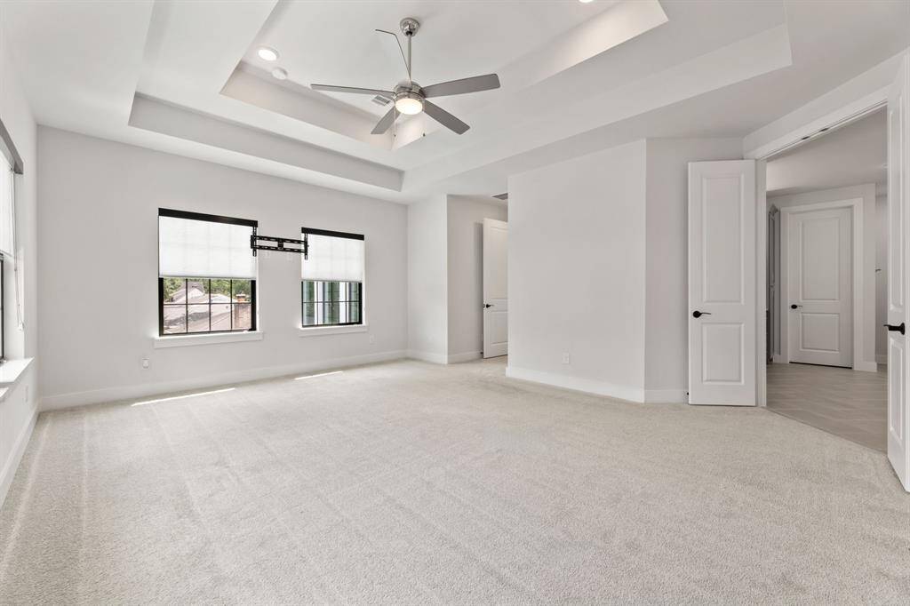 Spacious primary bedroom featuring plush carpeting, a stylish double tray ceiling with a modern fan, and abundant natural light. Direct access to a luxurious ensuite bathroom enhances comfort and convenience.