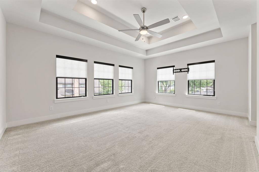 Spacious primary bedroom featuring plush carpeting, a stylish double tray ceiling with a modern fan, and abundant natural light. Direct access to a luxurious ensuite bathroom enhances comfort and convenience.