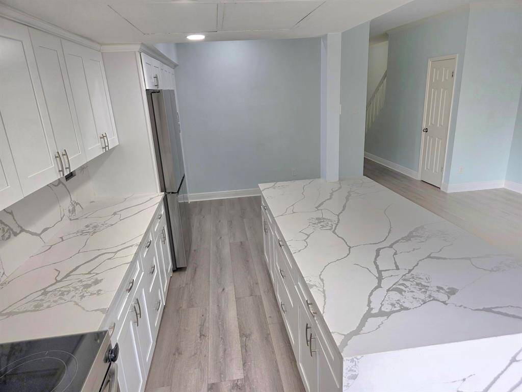 This photo showcases a modern open-plan kitchen and living area. It features sleek stainless steel appliances, a large island with marble countertops, and light wood flooring. The space is brightened by natural light from large windows and a sliding glass door leading to a fenced yard.