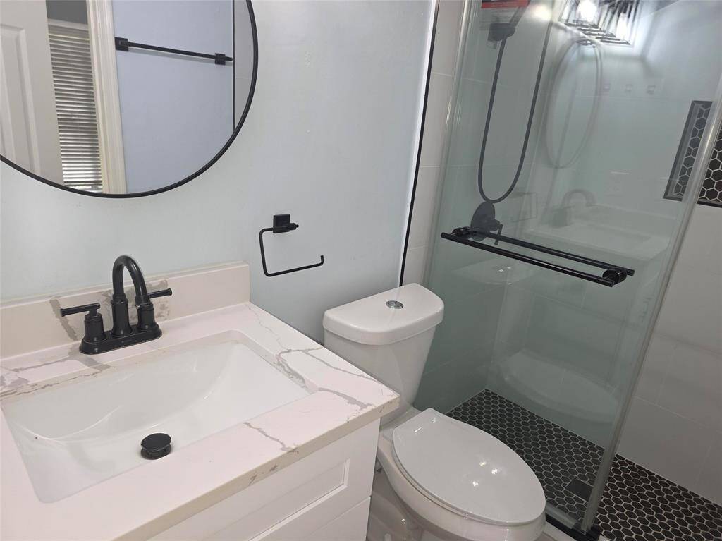 This bathroom features a modern design with a sleek vanity, black fixtures, and a round mirror. It includes a glass-enclosed shower with stylish hexagonal floor tiles, offering a clean and contemporary look.