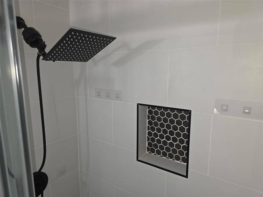 Modern shower with sleek black fixtures and a large rainfall showerhead. The wall features a stylish built-in niche with black hexagonal tiles for added elegance.