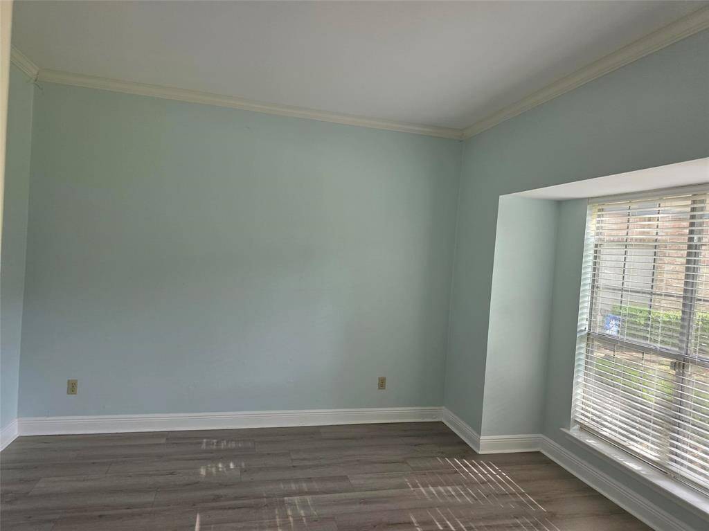 This room features light blue walls and a large window with blinds, allowing natural light to fill the space. It has modern wood flooring and a clean, simple design.