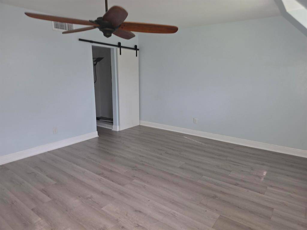 This room features light gray laminate flooring, pale blue walls, and a ceiling fan with wooden blades. A sliding barn door leads to an adjacent space, adding a modern touch.