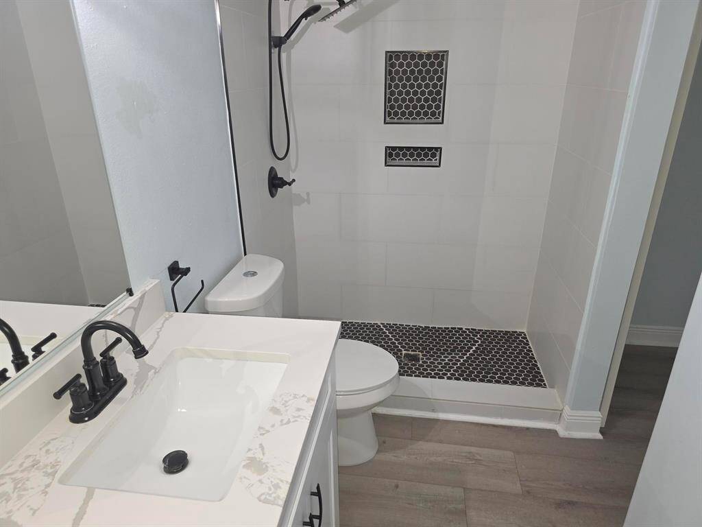 This bathroom features a modern design with a sleek shower area, black hexagonal tile accents, a white vanity with black fixtures, and light wood-style flooring.