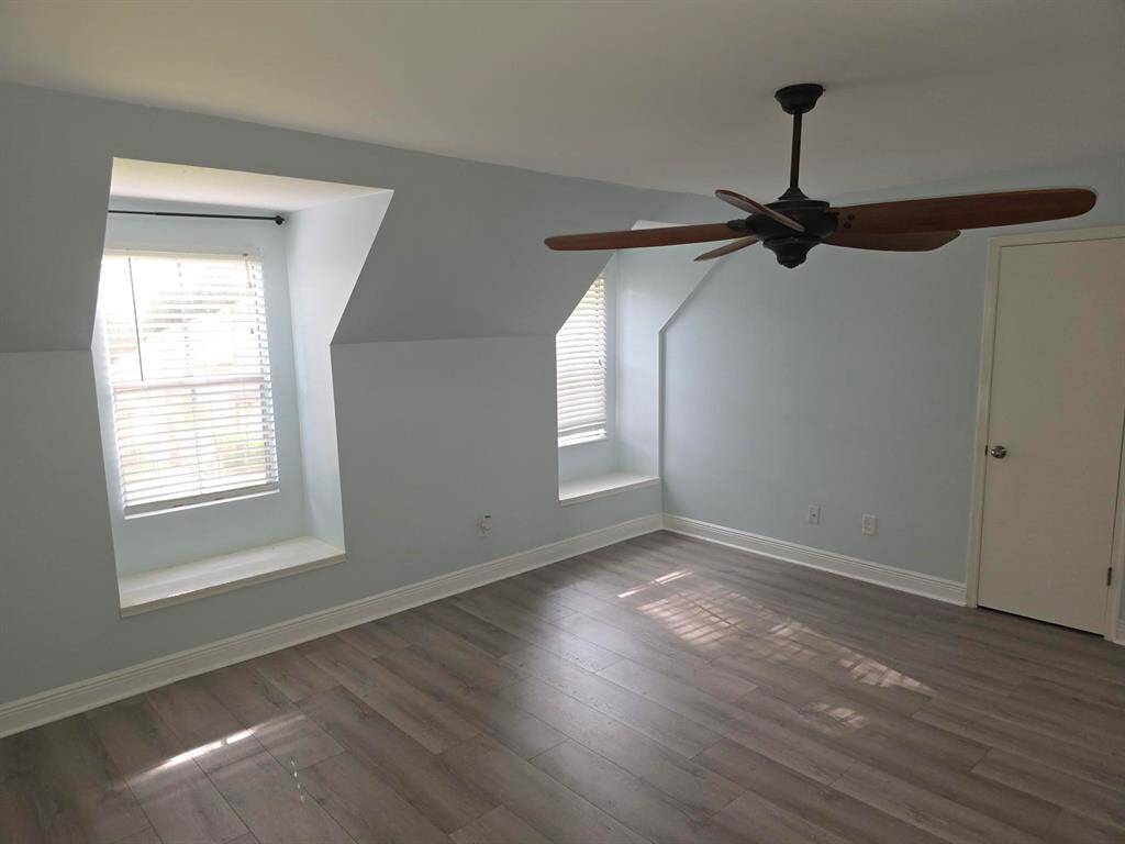 This bright room features light blue walls, two charming dormer windows with built-in seating, and sleek hardwood floors. A modern ceiling fan is centrally placed, enhancing the airy feel.