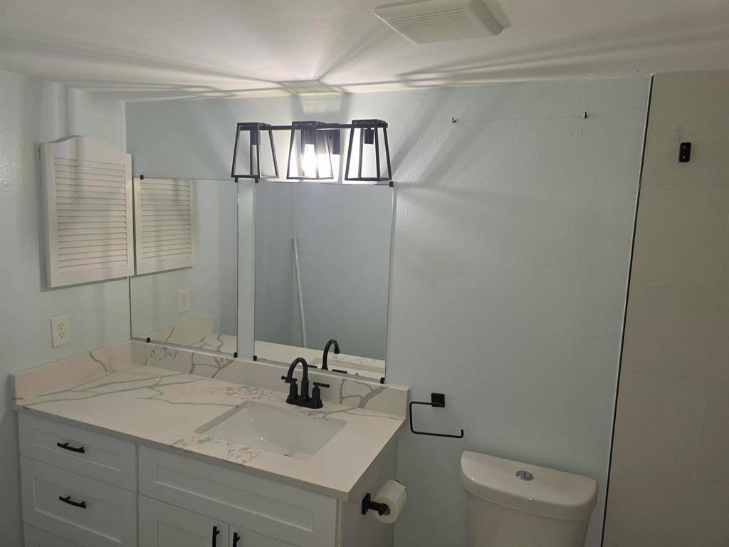 This bathroom features a modern sink with a sleek black faucet, a large mirror, and stylish overhead lighting. It has a white vanity with ample storage and a light, airy feel, complemented by soft wall colors.