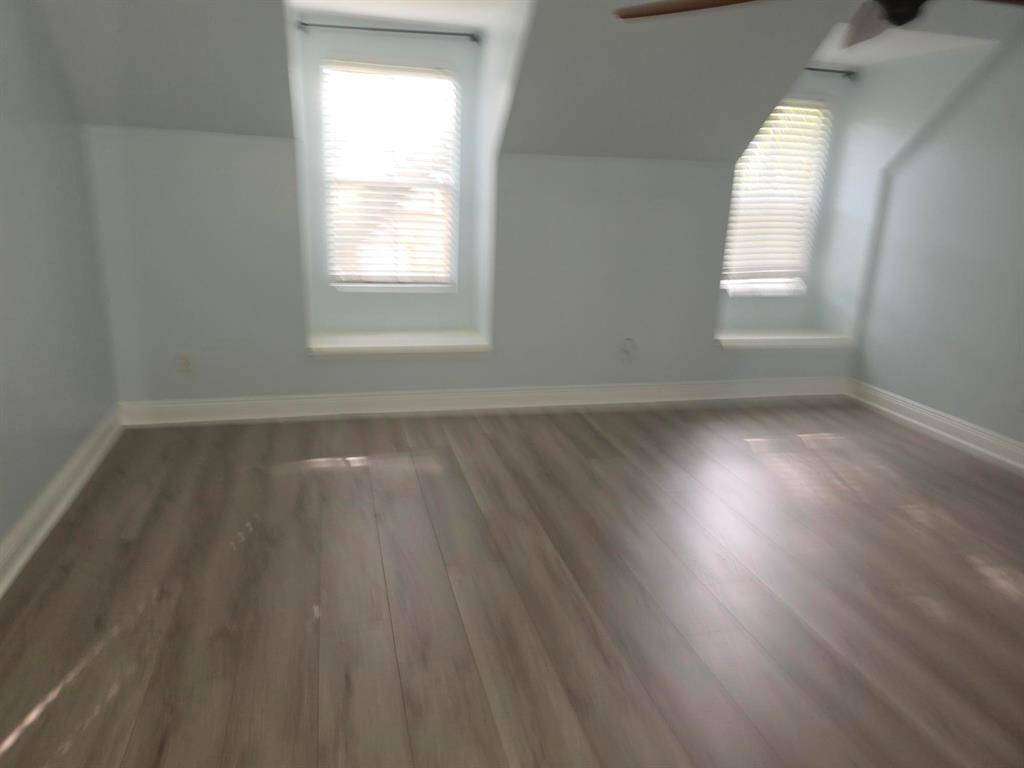 Bright, airy room with two windows, light blue walls, and sleek wood flooring. Great for a bedroom or office.