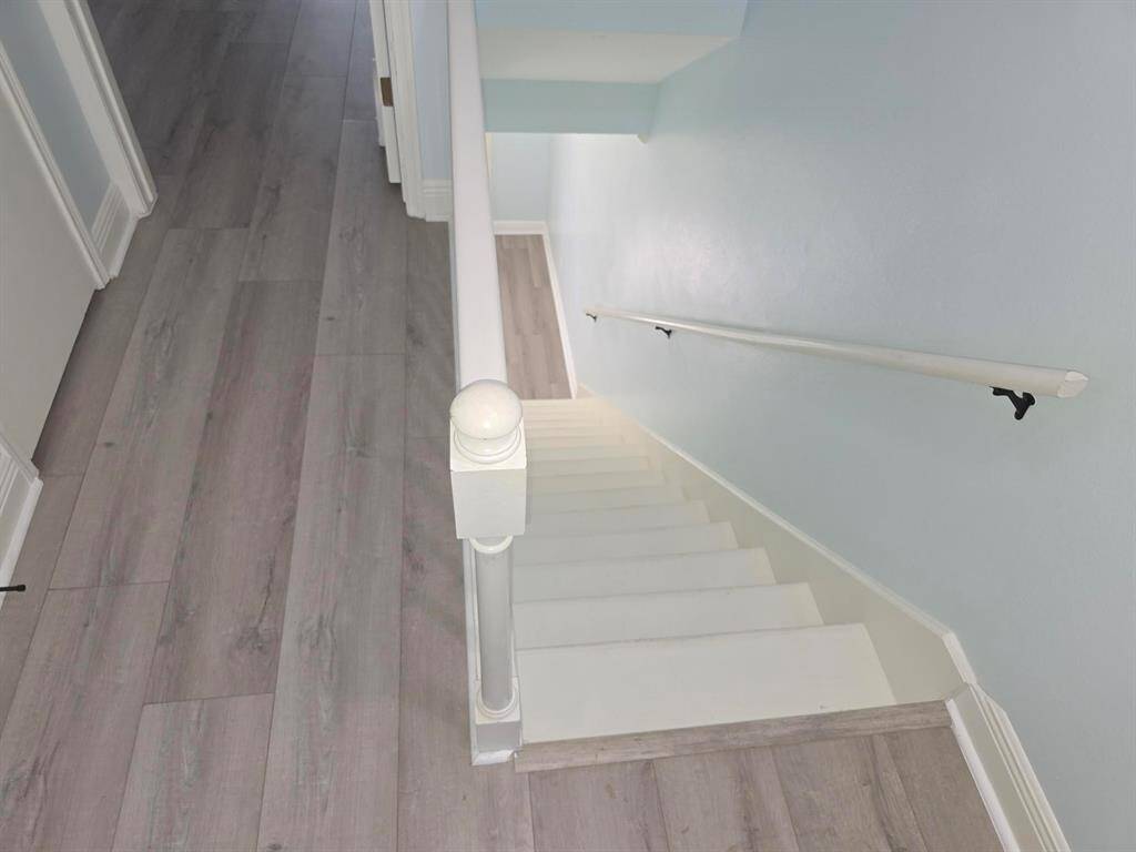 This photo shows a staircase with light-colored wood flooring and walls painted in a soft blue. The stair railing is white, complementing the clean and modern aesthetic.