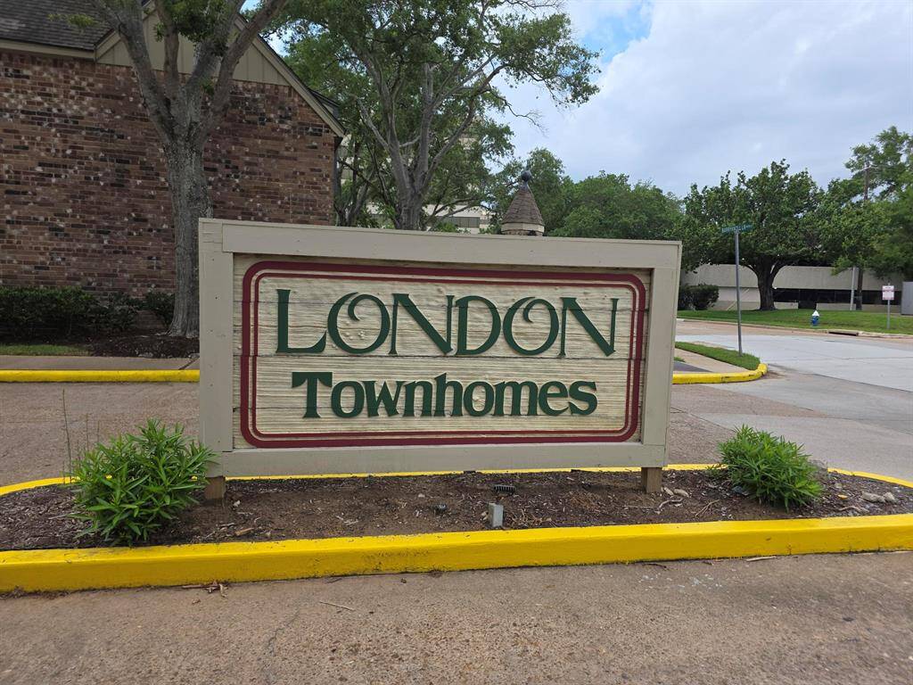 This photo shows the entrance sign for London Townhomes, surrounded by greenery and set on a well-maintained street. The area appears quiet and residential.