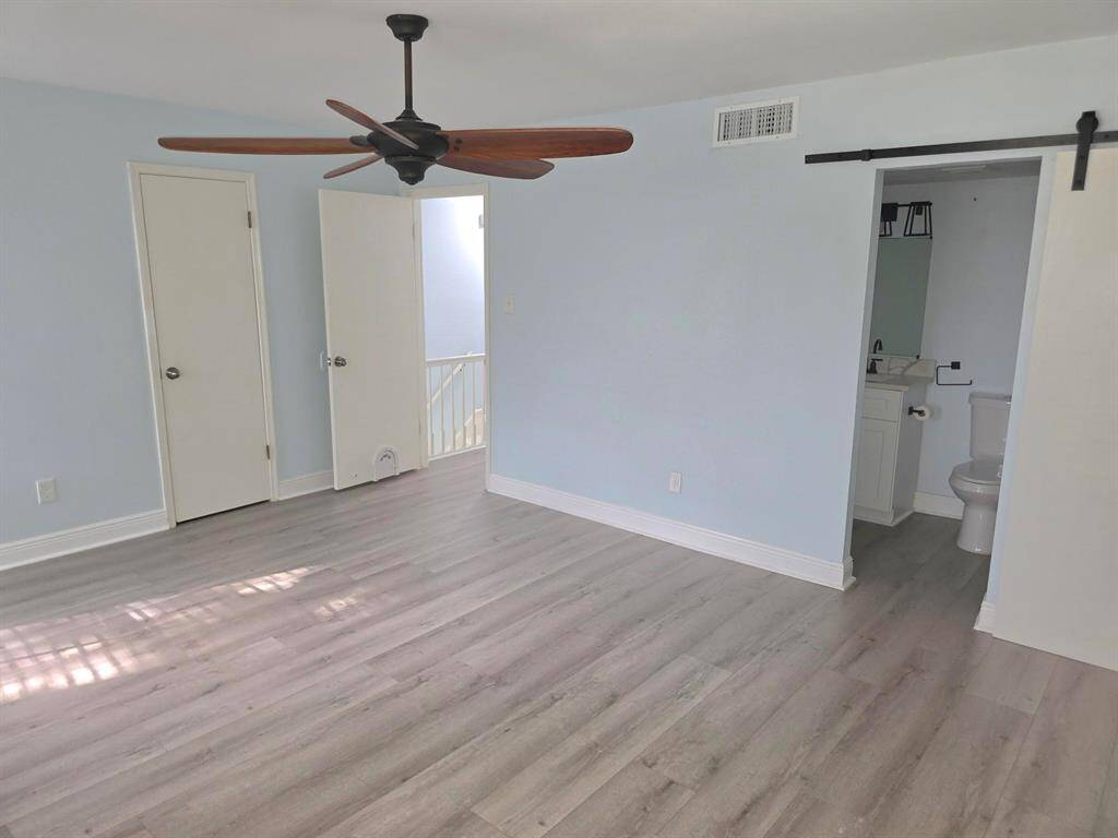 This photo showcases a modern open-plan kitchen and living area. It features sleek stainless steel appliances, a large island with marble countertops, and light wood flooring. The space is brightened by natural light from large windows and a sliding glass door leading to a fenced yard.