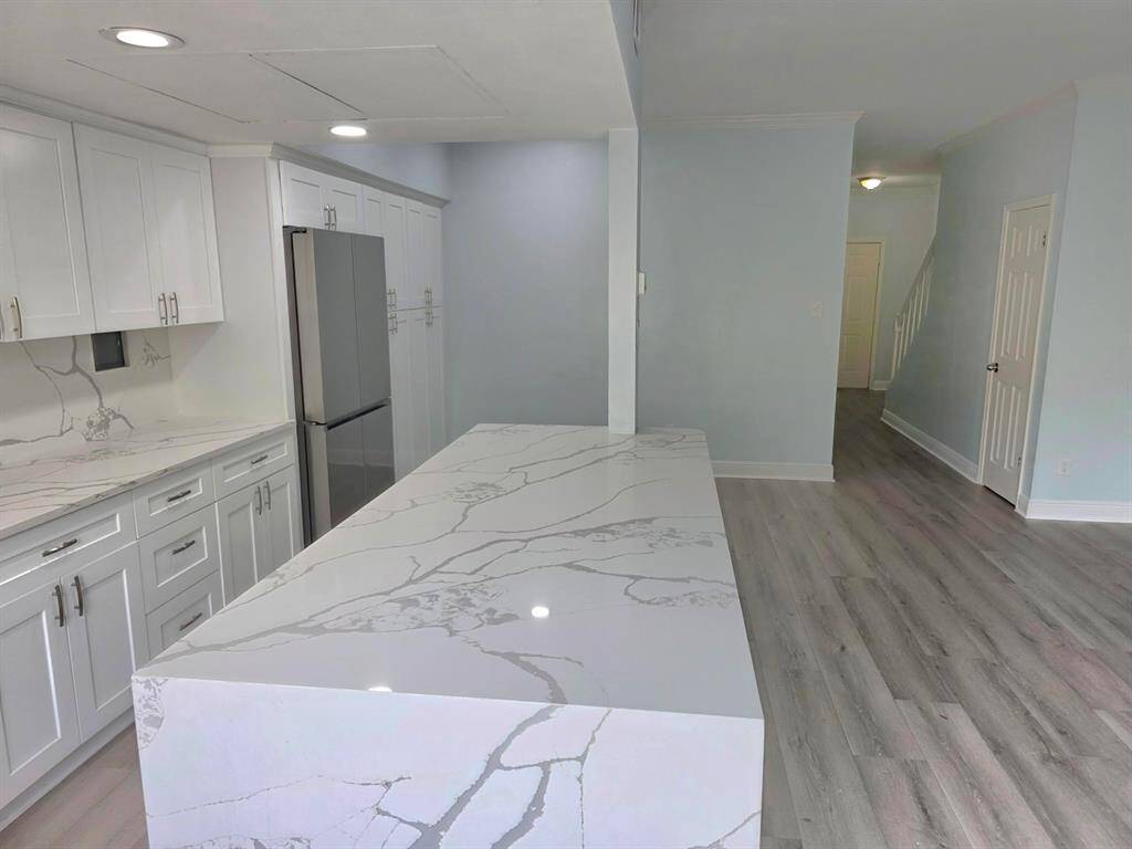 This photo showcases a modern open-plan kitchen and living area. It features sleek stainless steel appliances, a large island with marble countertops, and light wood flooring. The space is brightened by natural light from large windows and a sliding glass door leading to a fenced yard.
