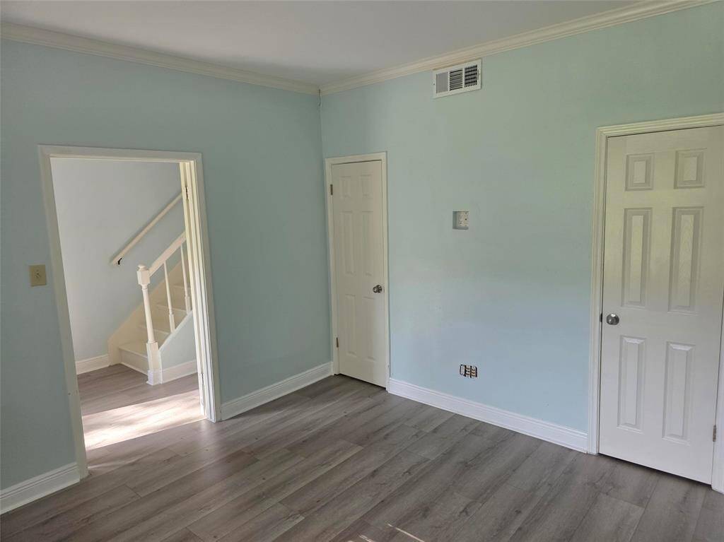 This room features light blue walls, two doors, and laminate flooring. It has a view of a staircase through an open doorway, offering a bright and open feel.