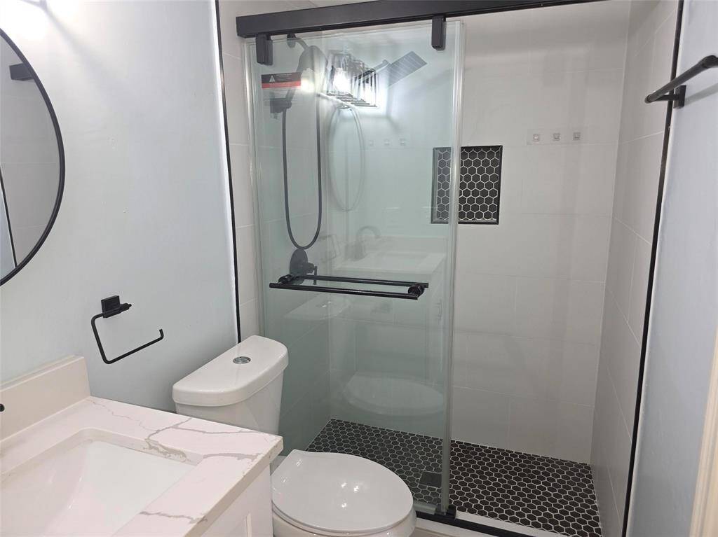 Modern bathroom featuring a sleek glass-enclosed shower with dark hexagonal tiles and a built-in niche. It includes a contemporary vanity with a marble-look countertop and a round mirror.