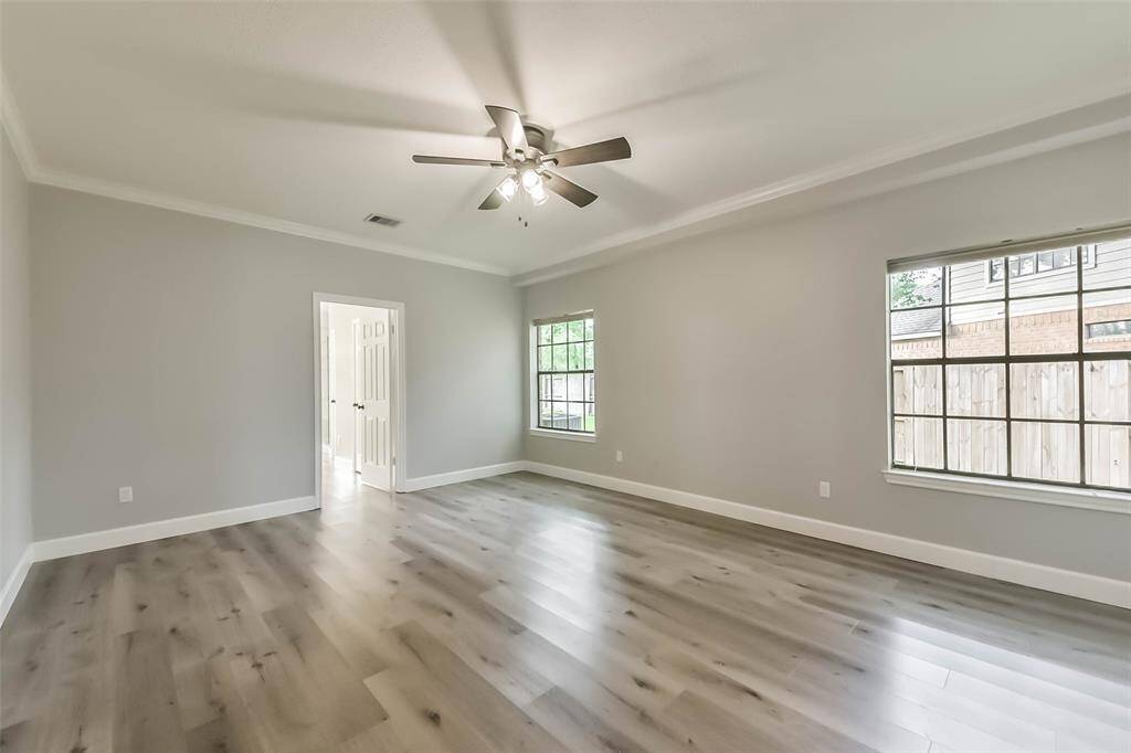 This spacious primary bedroom offers a serene retreat with soft neutral tones and elegant crown molding. The room features large windows that provide natural light and a view of the backyard. A ceiling fan adds comfort, while the ensuite bath is conveniently accessed through a private entry. With plenty of room for a king-sized bed and additional furnishings, this space is both relaxing and functional.