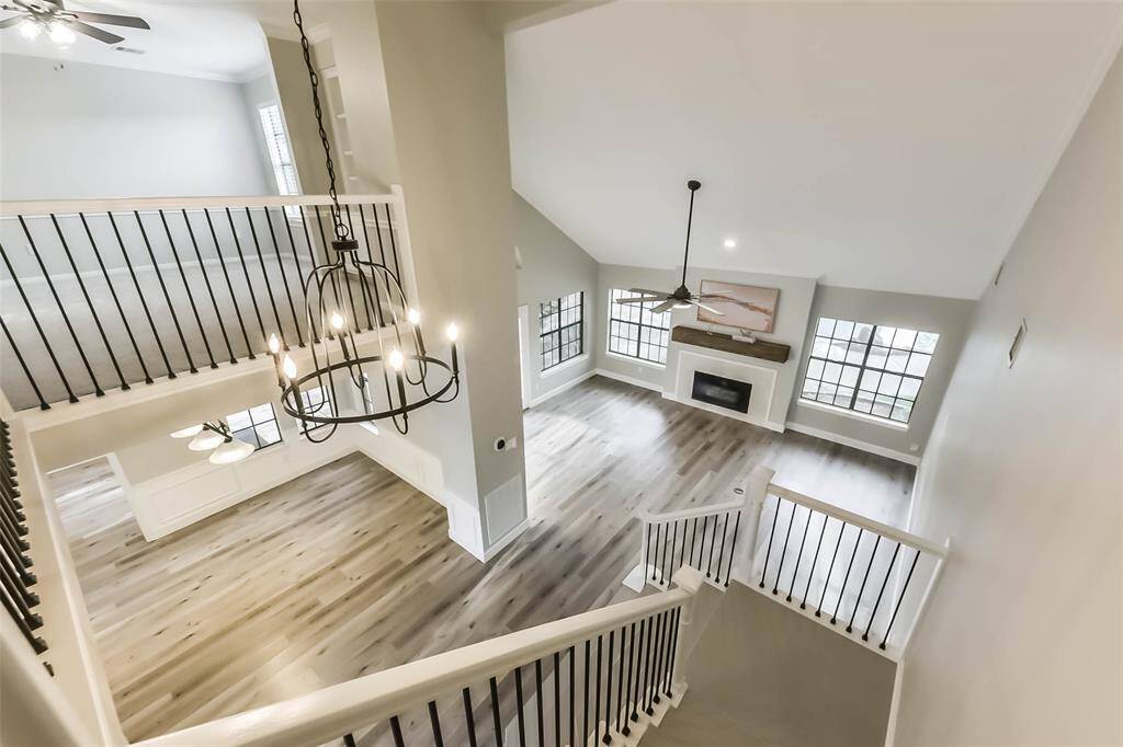 Enjoy a stunning view from the upstairs landing overlooking the open-concept living area, complete with soaring ceilings and an abundance of natural light. The elegant chandelier and modern stair railings add a touch of sophistication to the space. This layout creates a seamless flow between both levels, perfect for entertaining and everyday living. The large windows and cozy fireplace below make the living area feel warm and inviting. Virtually staged.