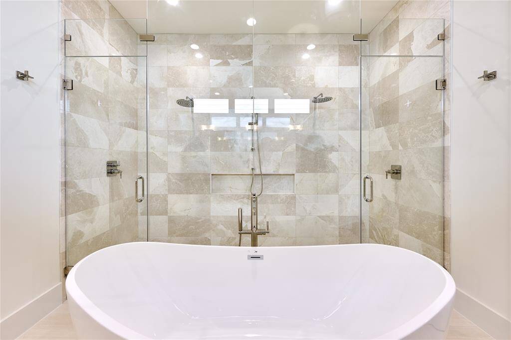Walk-in shower with dual shower heads, finished in sleek limestone tile and marble mosaic.