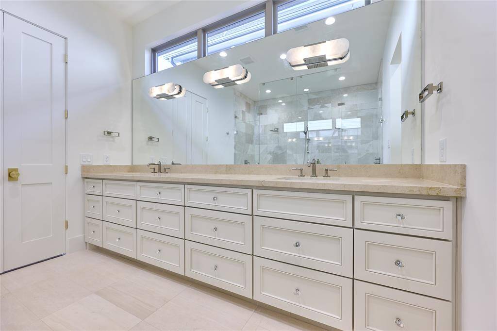 This spacious bathroom features a large double vanity with ample storage, elegant light fixtures, and a modern walk-in shower with glass doors.