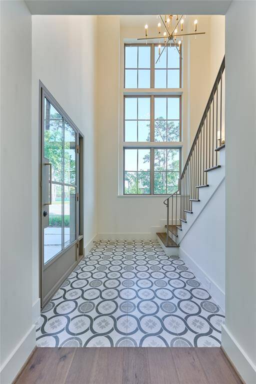 This entryway features a high ceiling with large windows, patterned tile flooring, and a modern chandelier.